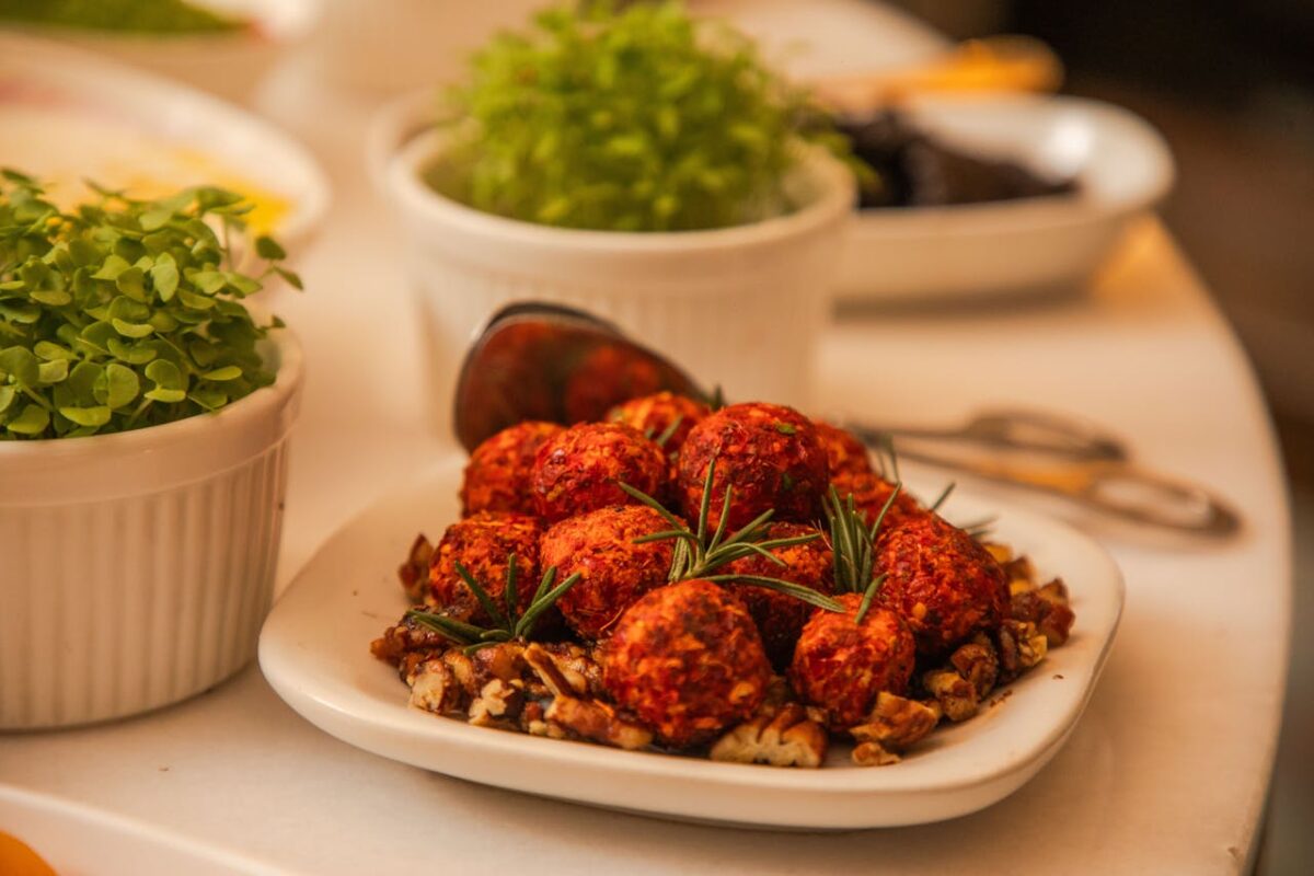 Close-up of spicy cheese balls garnished with rosemary and nuts, surrounded by fresh herbs.