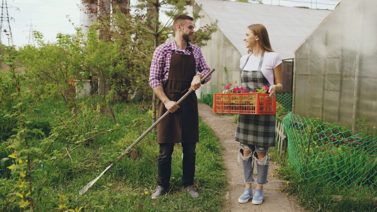 Two young gardeners sharing tasks outside a greenhouse, tending plants.